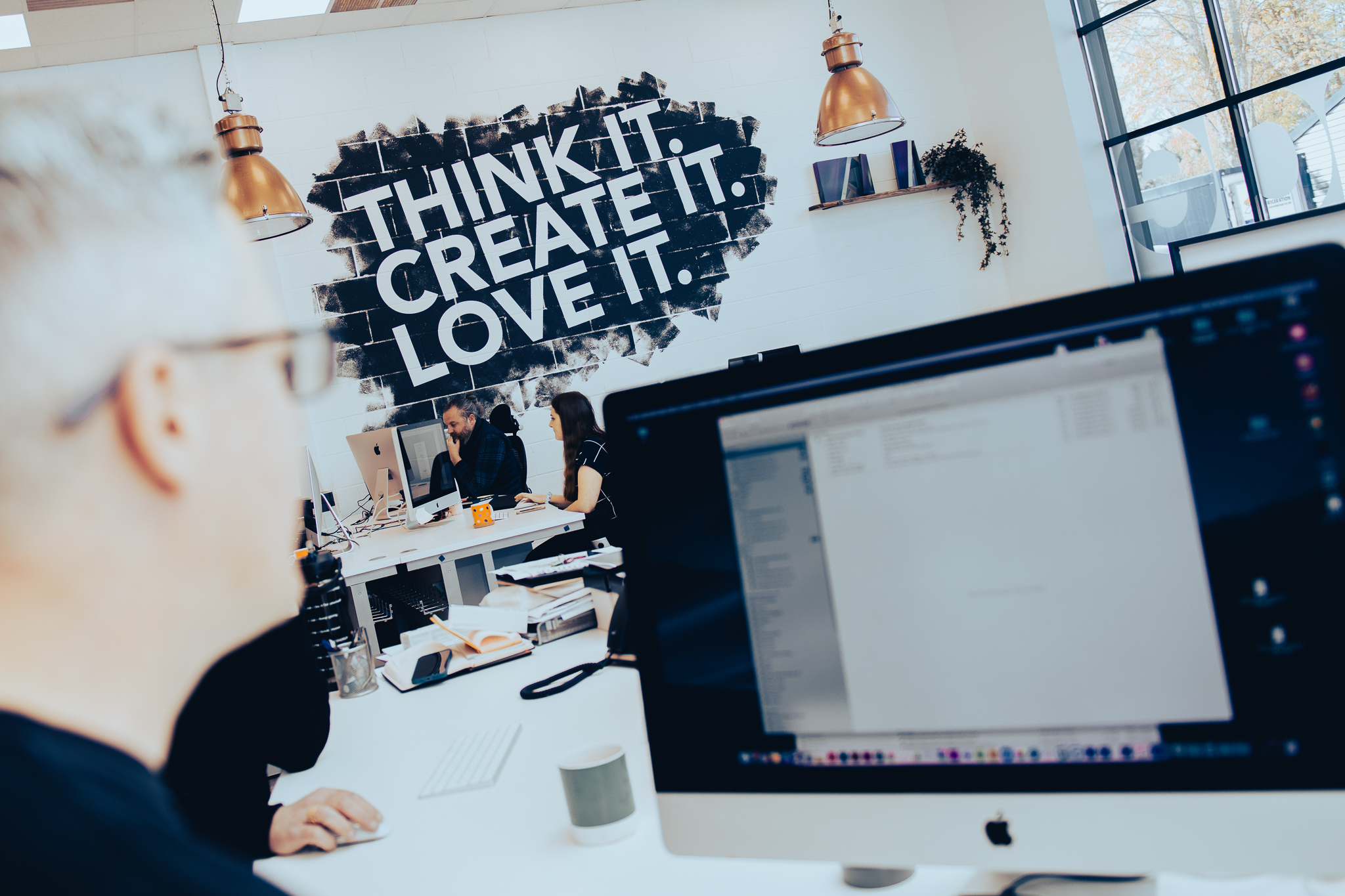 A man sitting in a studio with the caption: Think it. Create it. Love it. on the wall.